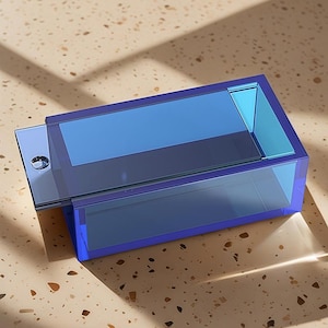 Può includere: Una scatola rettangolare blu trasparente con un coperchio scorrevole. La scatola è realizzata in un materiale trasparente, che permette il passaggio della luce. Il coperchio è di una tonalità di blu più scura e la scatola è su una superficie maculata.