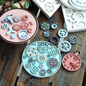May include: A set of silicone moulds for making various shapes of gears and a pocket watch. The moulds are on a wooden surface with some of the moulds filled with blue and pink resin.