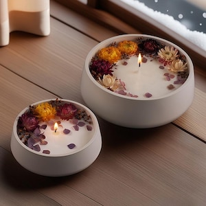 Puede incluir: Dos cuencos de cerámica blanca con una vela blanca en el centro de cada uno. Los cuencos están llenos de flores secas y cristales. Las velas están encendidas.