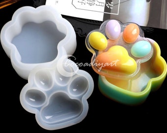 Può includere: Due stampi in silicone a forma di impronta di zampa. Uno stampo è una singola impronta di zampa, l'altro è un'impronta di zampa con quattro impronte di zampa più piccole all'interno. Gli stampi sono bianchi e traslucidi.
