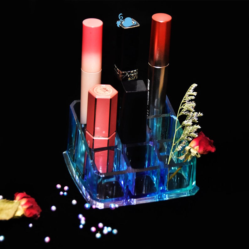 May include: A clear blue acrylic makeup organizer with multiple compartments to hold lipstick, lip gloss, and other makeup items. The organizer is filled with various shades of lipstick and lip gloss.