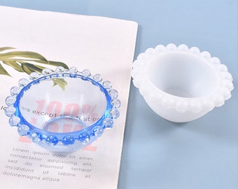 May include: Two small bowls, one blue glass with a beaded rim and one white silicone with a beaded rim.