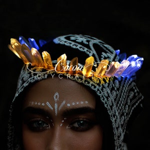 May include: A person wearing a black and white patterned head covering with a crown of glowing blue and yellow crystal-shaped lights. The text "Cocoa DIY Crafts" is visible on the head covering.
