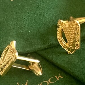 May include: A pair of gold cufflinks featuring a detailed design of a harp, the national symbol of Ireland. The cufflinks are displayed on a green velvet background with the text "Castle Knock Designs" printed on the surface.