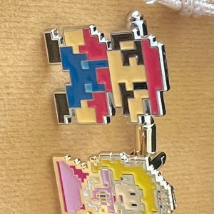 May include: Two pixelated character pins, one red and blue and the other yellow and pink. The red and blue pin is of a character with a red hat and blue overalls. The yellow and pink pin is of a character with a yellow dress and pink hair.