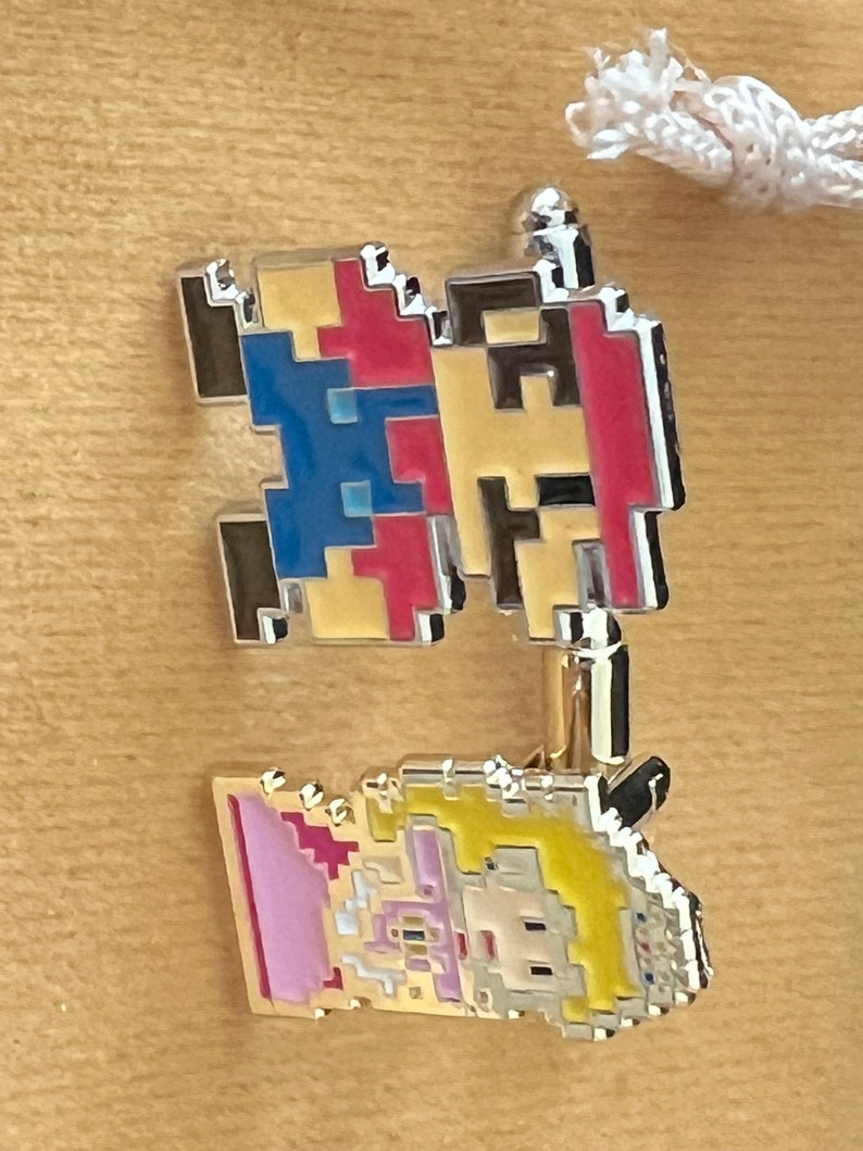 May include: Two pixelated character pins, one red and blue and the other yellow and pink. The red and blue pin is of a character with a red hat and blue overalls. The yellow and pink pin is of a character with a yellow dress and pink hair.