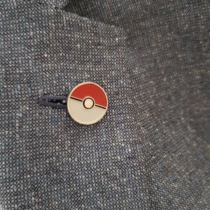 May include: A red and white Pokeball pin on a blue fabric background.