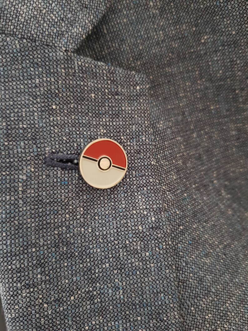 May include: A red and white Pokeball pin on a blue fabric background.