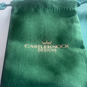 May include: A green velvet drawstring pouch with a gold logo that reads "CASTLEKNOCK DESIGNS" with a crown above the word "CASTLEKNOCK".
