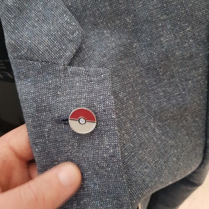 May include: A blue denim jacket with a silver and red Pokeball pin on the left side.