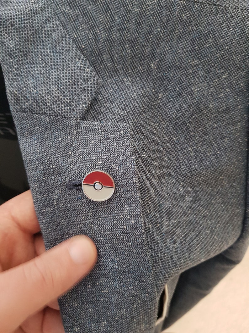 May include: A blue denim jacket with a silver and red Pokeball pin on the left side.