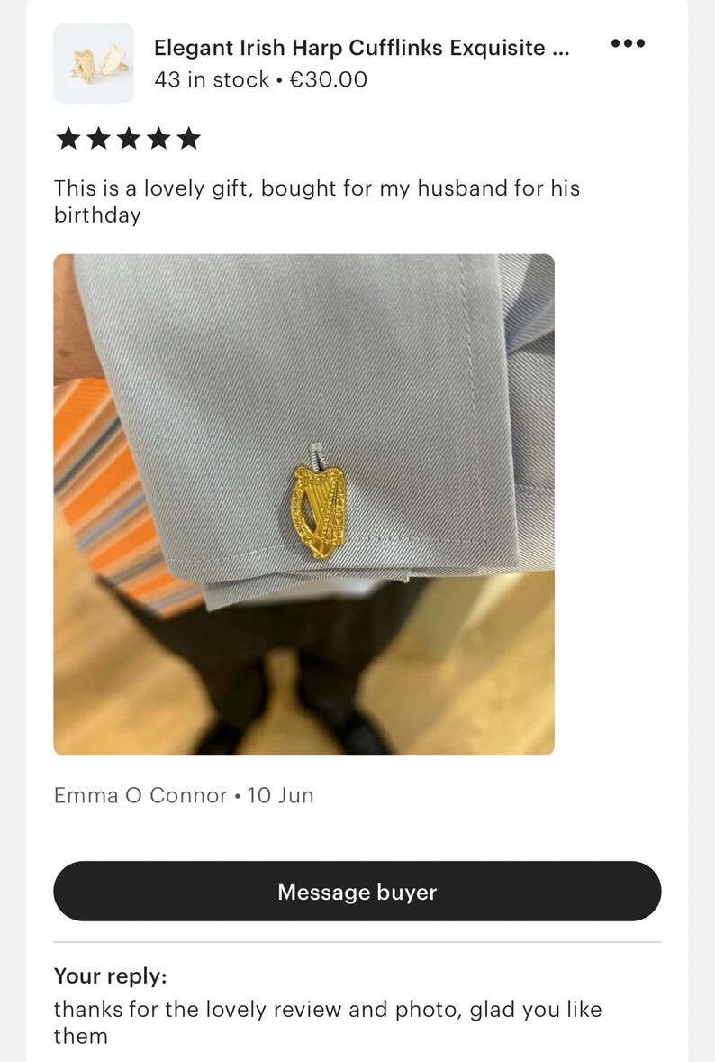 May include: Gold-coloured cufflinks featuring a detailed harp design. The cufflinks are shown on a light blue shirt with a striped orange and white tie.