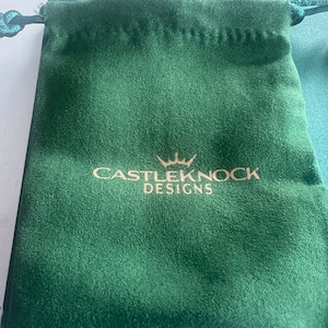May include: A green velvet drawstring pouch with a gold logo that reads "CASTLEKNOCK DESIGNS" with a crown above the word "CASTLEKNOCK".