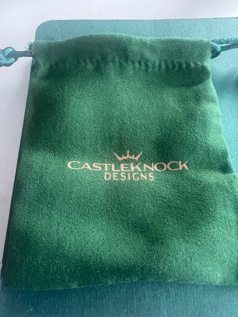 May include: A green velvet drawstring pouch with a gold logo that reads "CASTLEKNOCK DESIGNS" with a crown above the word "CASTLEKNOCK".