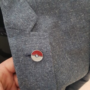 May include: A blue fabric jacket with a silver and red Pokeball pin.