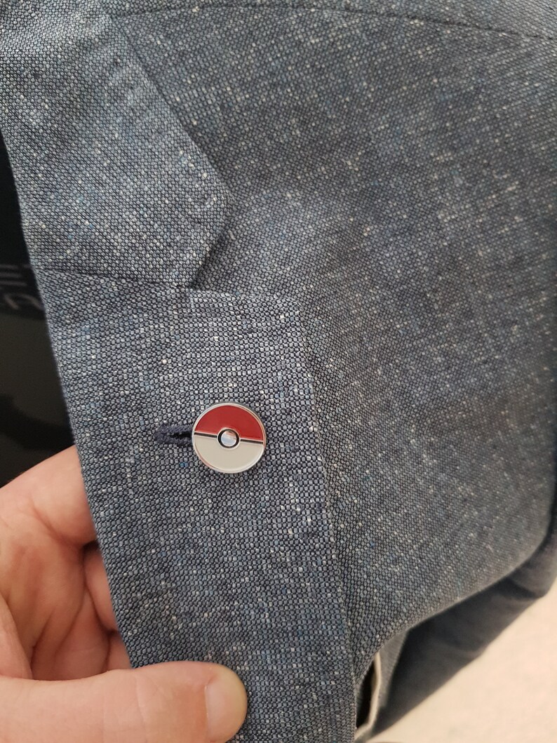 May include: A blue fabric jacket with a silver and red Pokeball pin.