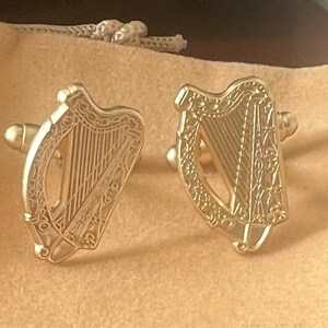 May include: A pair of gold cufflinks featuring a detailed design of a harp, the national symbol of Ireland.