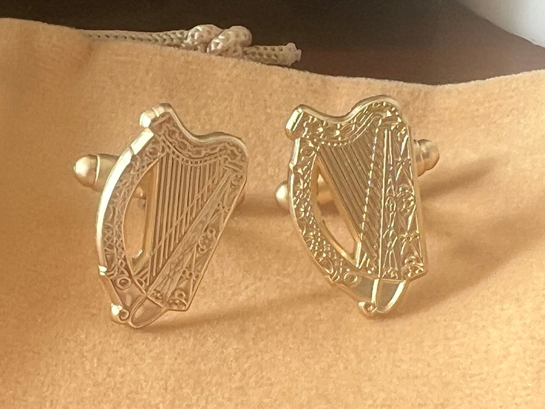 May include: A pair of gold cufflinks featuring a detailed design of a harp, the national symbol of Ireland.