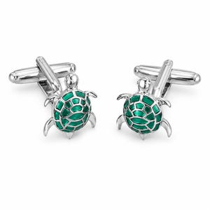 Può includere: Un paio di gemelli in metallo color argento con un design a forma di tartaruga marina. Ogni tartaruga presenta testa e arti in argento lucido con un guscio in smalto verde brillante che mostra un motivo segmentato dettagliato.