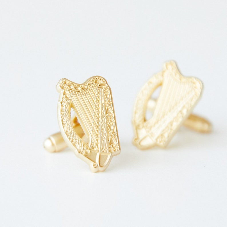 May include: A pair of gold cufflinks featuring a detailed design of a Celtic harp. The cufflinks are a traditional Irish symbol.