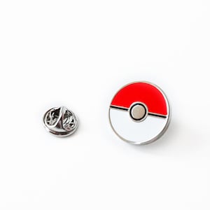 May include: A silver metal pin with a red and white Pokeball design. The pin has a silver metal clasp on the back.