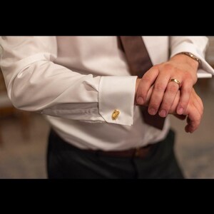 May include: A white dress shirt with gold cufflinks. The shirt is buttoned at the cuff and the cufflinks are visible.