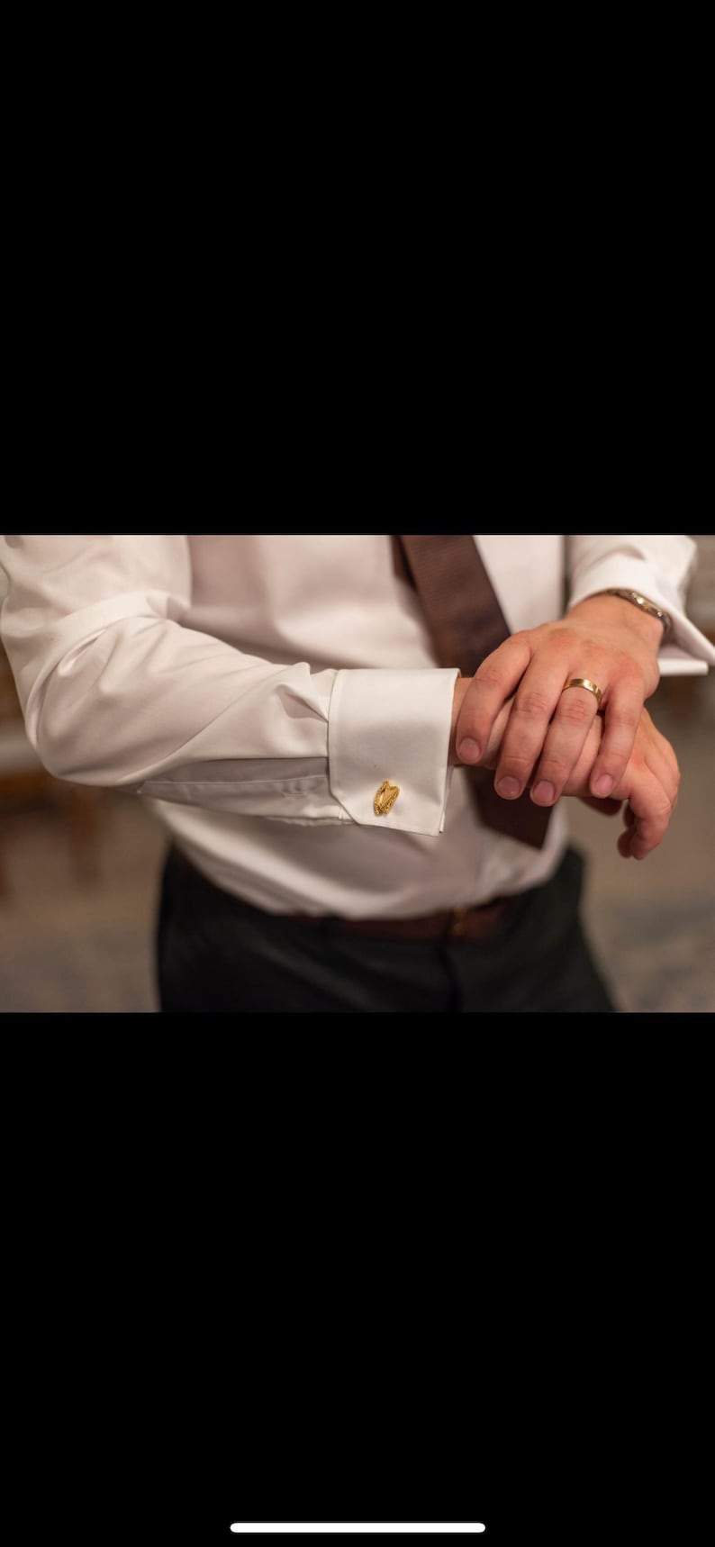 May include: A white dress shirt with gold cufflinks. The shirt is buttoned at the cuff and the cufflinks are visible.