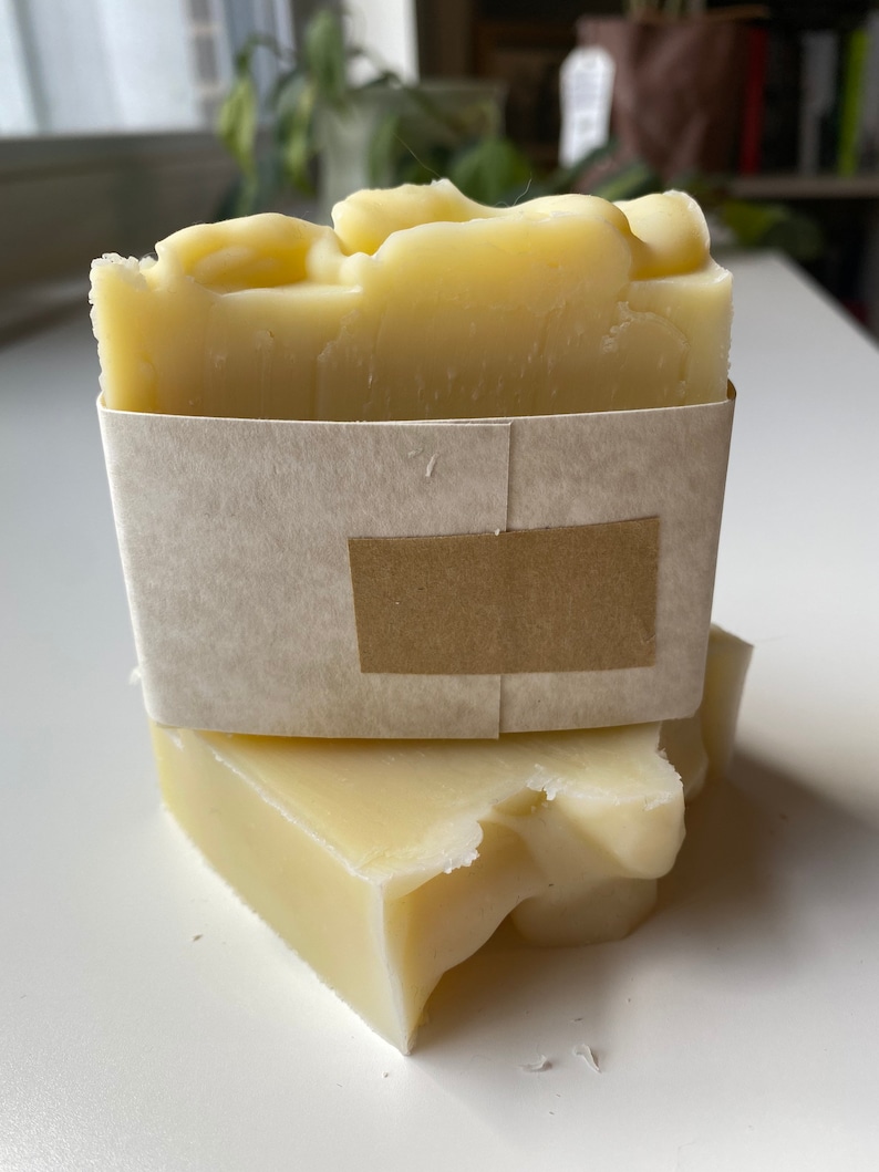 May include: Two bars of handmade soap wrapped in brown paper. The soap is a pale yellow colour and has a rough texture.