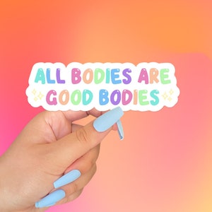May include: A white sticker with the text "ALL BODIES ARE GOOD BODIES" in rainbow colors. The sticker has a white border and is held by a hand with light blue nail polish.