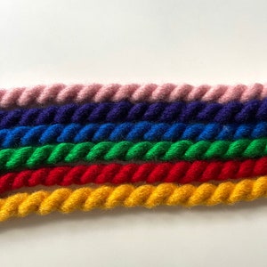 May include: Five strands of colorful yarn are twisted together in a rope-like pattern. The colors are pink, blue, green, red, and yellow.
