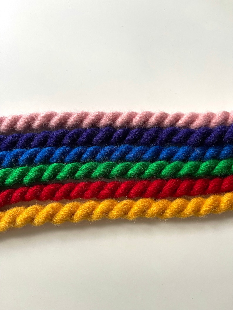 May include: Five strands of colorful yarn are twisted together in a rope-like pattern. The colors are pink, blue, green, red, and yellow.