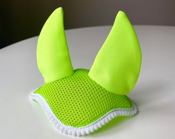 Könnte beinhalten: Ein leuchtend neongrüner Fliegenhaube für Pferde mit weißem Besatz. Die Haube hat ein Netzdesign und zwei große Ohrenklappen.