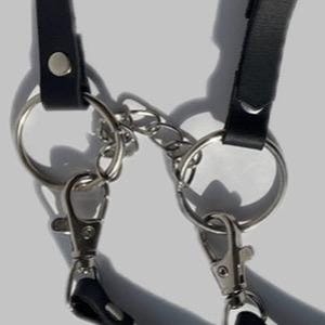 May include: Close-up of a black leather strap with two silver key rings and a silver chain connecting them.