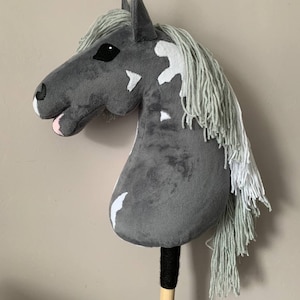 May include: A gray and white spotted plush horse head with a long, gray mane. The horse head is attached to a wooden stick.