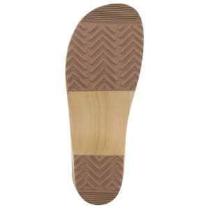 May include: The bottom of a wooden clog with a brown rubber sole. The sole has a chevron pattern.