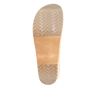 May include: The bottom of a wooden clog with a brown leather sole. The sole has a chevron pattern.