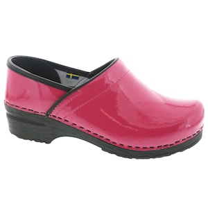 May include: Pink patent leather clogs with a black rubber sole and a black stitched seam around the edge.