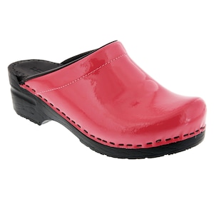 May include: A glossy, bright red clog shoe with a black sole and heel. The shoe features a rounded toe and a stitched design along the sole. The upper is a shiny, patent leather-like material. The heel is approximately 2 inches high.