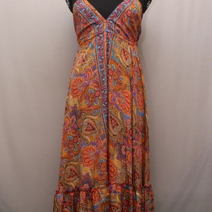 Può includere: Un lungo abito da sera con scollo a halter e stampa paisley in tonalità arancio, blu e rosa. L'abito ha un orlo a balze e una chiusura con bottoni sul davanti.