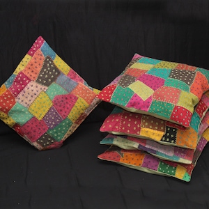 Op de afbeelding: Een stapel van vijf kleurrijke patchwork kussens met verschillende kleuren en patronen, waaronder roze, groen, geel en bruin.