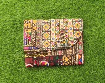Pode incluir: Uma carteira de mão colorida em patchwork com bordados intrincados e fecho de aba. A carteira é feita de vários tecidos em tons de marrom, amarelo, vermelho, azul e verde.