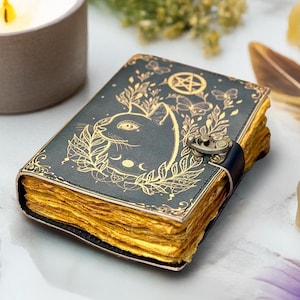 May include: A dark green leather journal with a cat design and gold accents. The cover features a cat silhouette, botanical elements, and a pentagram. The pages have a golden hue, and the journal is secured with a clasp.