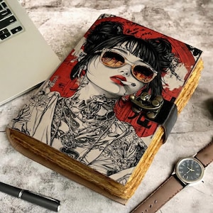 Könnte beinhalten: Ein Notizbuch im Vintage-Stil mit einer auffälligen Illustration einer Frau mit Sonnenbrille, Tätowierungen und einer Zigarette. Das Notizbuch hat einen Holzdeckel, einen Lederriemenverschluss und gealterte Papierseiten.