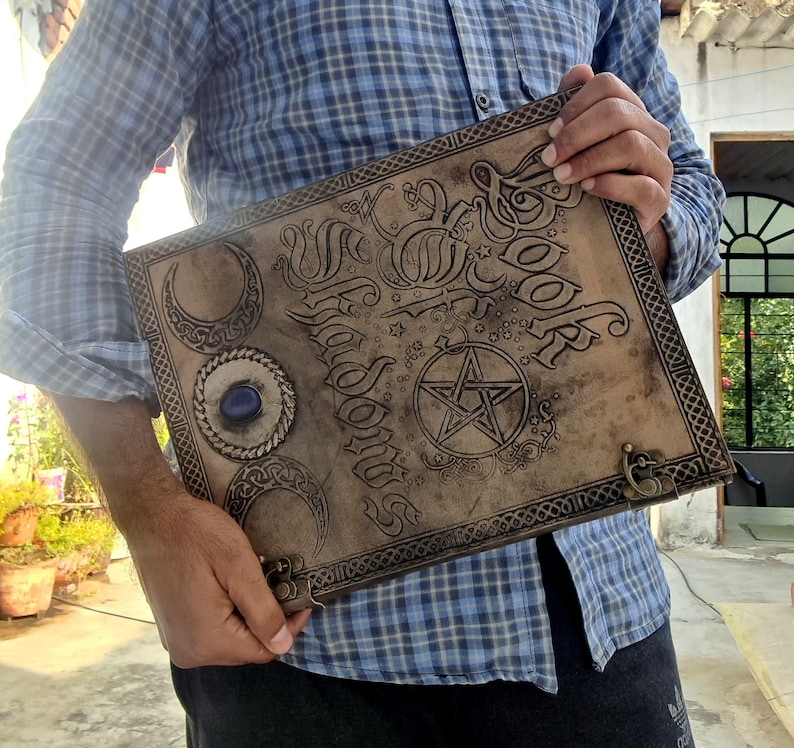 May include: A brown leather journal with a pentagram and the words "The Book of Shadows" embossed on the cover. The journal has a blue gemstone on the front.