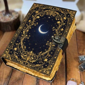 May include: A dark blue journal with a crescent moon and star design on the cover. The cover is adorned with gold floral patterns and a metal clasp. The pages have a vintage, aged appearance.