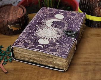 May include: A purple leather journal with a celestial design featuring a sun and moon with a clasp closure. The journal has a vintage look with aged paper pages.