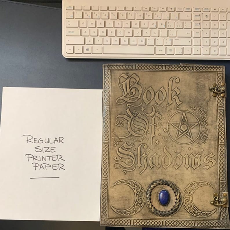 May include: A brown leather-bound journal with the words "Book of Shadows" embossed on the front cover. The cover also features a pentagram, three crescent moons, and a blue gemstone.