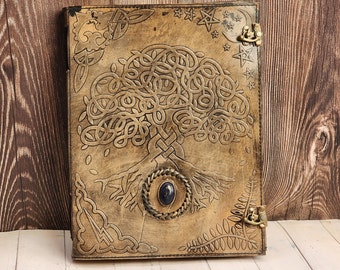 May include: A brown leather journal with a Celtic tree of life design and a blue gemstone embellishment. The journal has a metal clasp and is decorated with stars and moons.