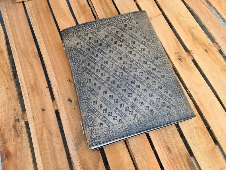 May include: A brown leather journal with a decorative embossed pattern. The pattern features a repeating geometric design with a floral border.