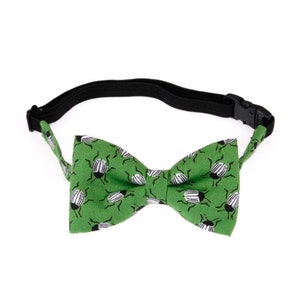 May include: A green bow tie with a black elastic band. The bow tie is covered in a pattern of black and white beetles.